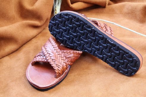 Pair of brown handwoven leather Moroccan sandals with crisscross braided straps, displayed on a warm suede background with barley spikes