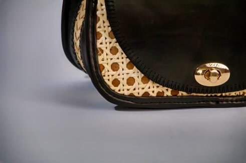 Chic handbag with black leather and woven cane accents, featuring a stylish round shape and gold clasp closure against a soft neutral background.