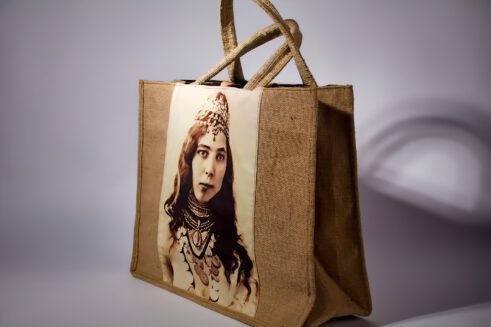 A handcrafted Moroccan tote bag featuring a vintage portrait print of a woman adorned with jewelry, placed on a neutral background surrounded by small stones.