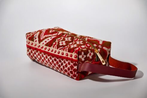 Handcrafted floral cosmetic pouch with a sturdy handle and vibrant red, brown, and cream patterns.