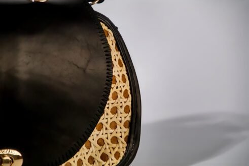 Chic handbag with black leather and woven cane accents, featuring a stylish round shape and gold clasp closure against a soft neutral background.