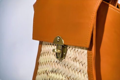 A stylish, handcrafted leather and woven material backpack with a brass clasp, set against a neutral background with a modern and elegant feel.