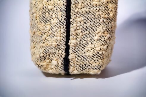 Handwoven beige cosmetic pouch with geometric patterns and a sturdy handle.