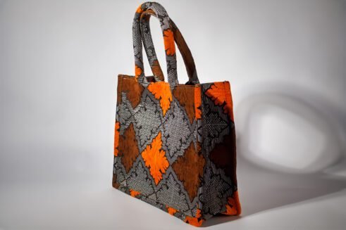 A handcrafted Moroccan tote bag featuring a geometric orange and black design, placed on a neutral background with a collection of colorful stones.
