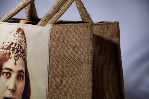 A handcrafted Moroccan tote bag featuring a vintage portrait print of a woman adorned with jewelry, placed on a neutral background surrounded by small stones.