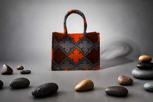 A handcrafted Moroccan tote bag featuring a geometric orange and black design, placed on a neutral background with a collection of colorful stones.