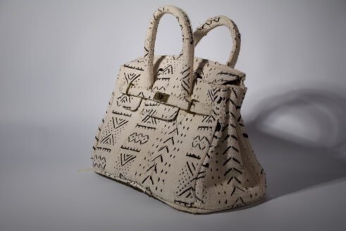 A handcrafted Moroccan tote bag with a tribal black geometric design on beige fabric, placed on a neutral background surrounded by small stones.