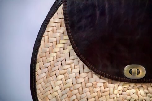 Classic handbag featuring a dark brown leather top and woven cane body, with a rounded silhouette and brass clasp closure, set against a neutral beige background.