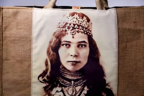 A handcrafted Moroccan tote bag featuring a vintage portrait print of a woman adorned with jewelry, placed on a neutral background surrounded by small stones.