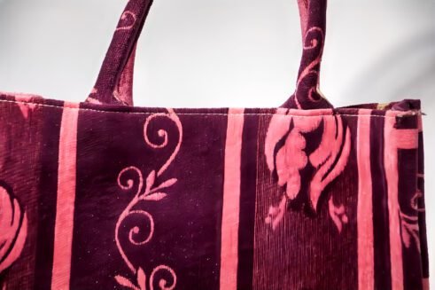 A handcrafted Moroccan tote bag with a floral design in purple and pink, placed on a neutral background surrounded by small stones.