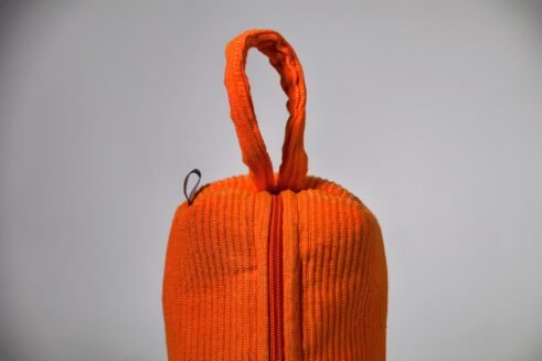 Orange cosmetic pouch with textured fabric and zipper, perfect for storing cosmetics and toiletries.