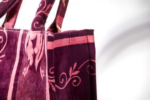 A handcrafted Moroccan tote bag with a floral design in purple and pink, placed on a neutral background surrounded by small stones.