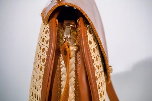 Elegant handbag with leather handles and woven cane material, showcasing a sleek and timeless design against a soft neutral background.