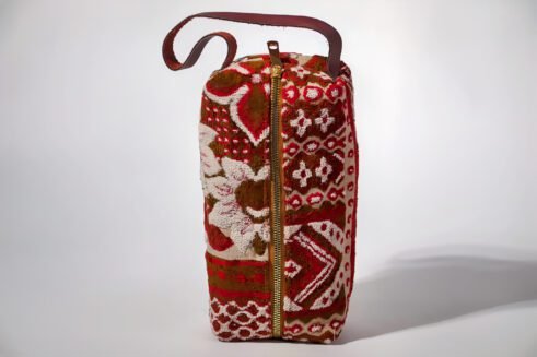 Handcrafted floral cosmetic pouch with a sturdy handle and vibrant red, brown, and cream patterns.