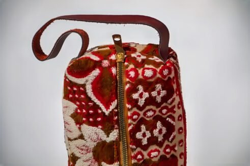 Handcrafted floral cosmetic pouch with a sturdy handle and vibrant red, brown, and cream patterns.