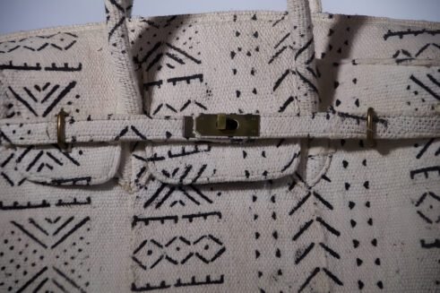 A handcrafted Moroccan tote bag with a tribal black geometric design on beige fabric, placed on a neutral background surrounded by small stones.