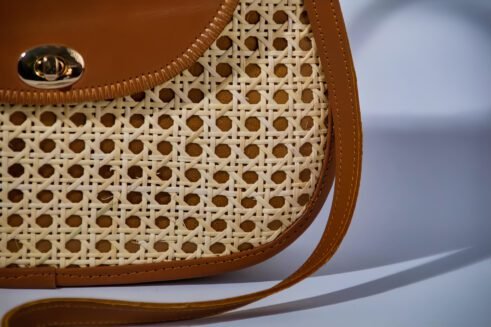 Elegant handbag with leather handles and woven cane material, showcasing a sleek and timeless design against a soft neutral background.