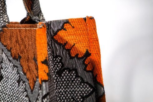 A handcrafted Moroccan tote bag featuring a geometric orange and black design, placed on a neutral background with a collection of colorful stones.