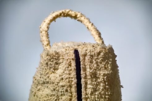 Handwoven beige cosmetic pouch with geometric patterns and a sturdy handle.