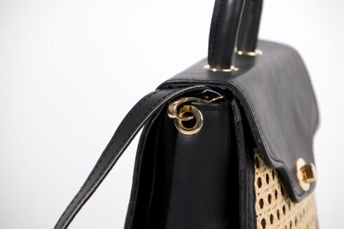 Chic handbag with a black leather top and woven cane body, featuring a gold-tone clasp, a sturdy handle, and an adjustable shoulder strap, styled against a soft neutral backdrop.