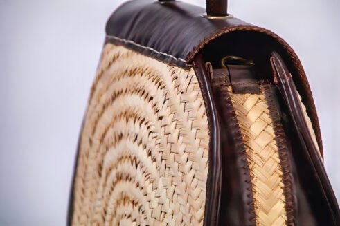 Chic handbag with black leather and woven cane accents, featuring a stylish round shape and gold clasp closure against a soft neutral background.