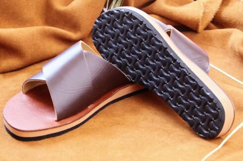 A pair of handmade Moroccan sandals featuring wide dark brown leather cross straps and stacked leather soles with a black rubber base, set on a camel suede background with wheat decor