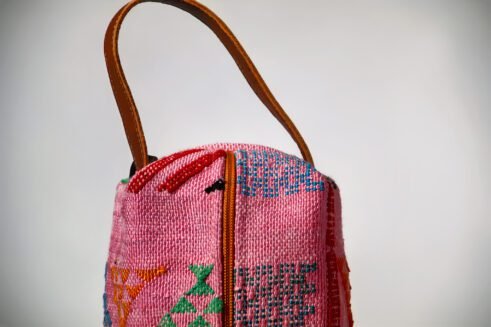 Colorful pink cosmetic pouch with geometric patterns and a small handle.