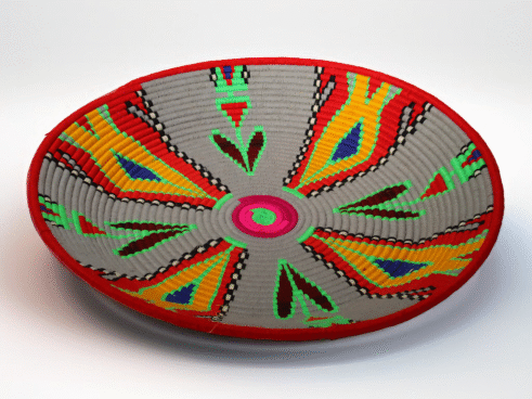 A beautifully handcrafted Moroccan coil basket with vibrant red, yellow, green, and blue geometric patterns, sitting on a white background surrounded by small stones.