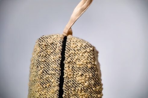 Handwoven beige cosmetic pouch with geometric patterns and a sturdy handle.