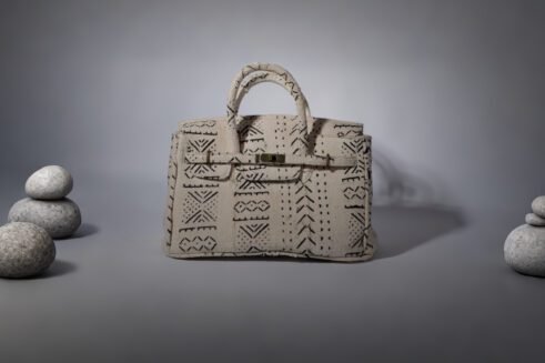 A handcrafted Moroccan tote bag with a tribal black geometric design on beige fabric, placed on a neutral background surrounded by small stones.