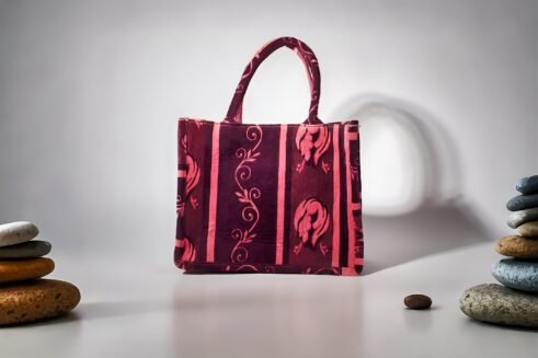 A handcrafted Moroccan tote bag with a floral design in purple and pink, placed on a neutral background surrounded by small stones.
