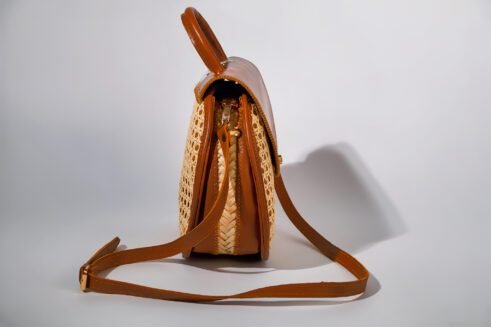 Elegant handbag with leather handles and woven cane material, showcasing a sleek and timeless design against a soft neutral background.