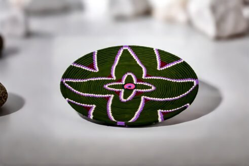 A handcrafted Moroccan coil basket with a green and purple floral design, surrounded by small stones on a neutral background.