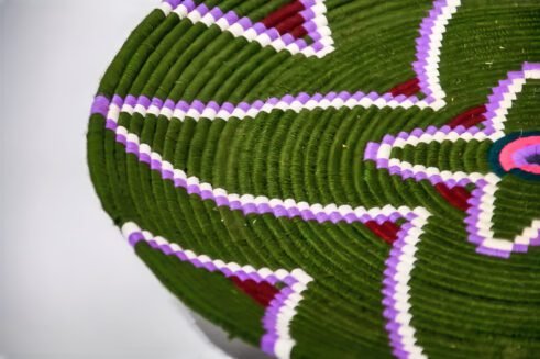 A handcrafted Moroccan coil basket with a green and purple floral design, surrounded by small stones on a neutral background.