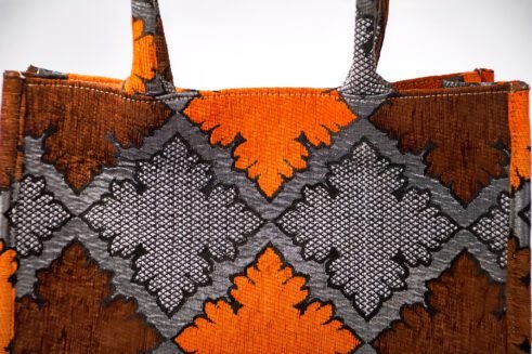 A handcrafted Moroccan tote bag featuring a geometric orange and black design, placed on a neutral background with a collection of colorful stones.