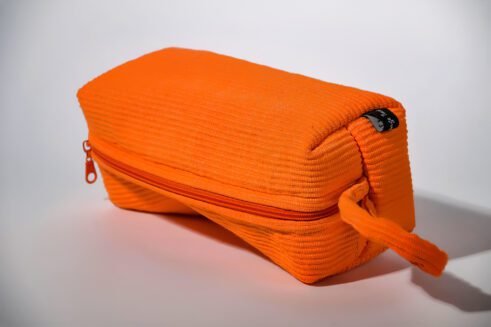 Orange cosmetic pouch with textured fabric and zipper, perfect for storing cosmetics and toiletries.