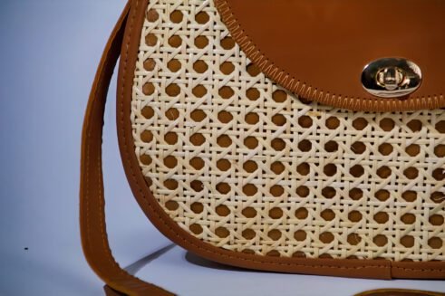 Elegant handbag with leather handles and woven cane material, showcasing a sleek and timeless design against a soft neutral background.