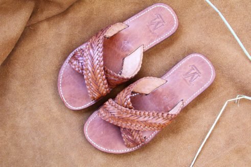 Pair of brown handwoven leather Moroccan sandals with crisscross braided straps, displayed on a warm suede background with barley spikes