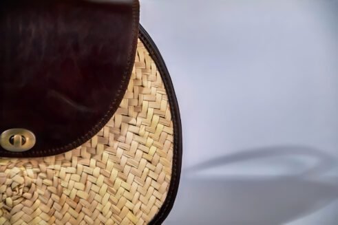 Classic handbag featuring a dark brown leather top and woven cane body, with a rounded silhouette and brass clasp closure, set against a neutral beige background.