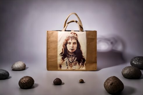 A handcrafted Moroccan tote bag featuring a vintage portrait print of a woman adorned with jewelry, placed on a neutral background surrounded by small stones.