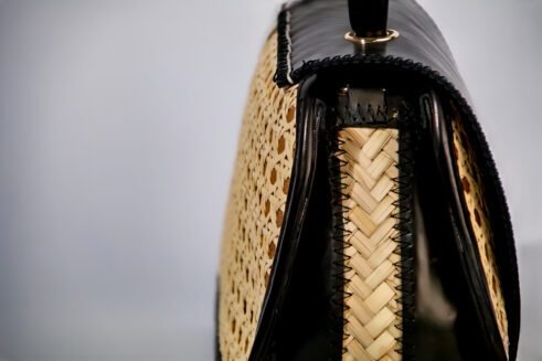 Chic handbag with black leather and woven cane accents, featuring a stylish round shape and gold clasp closure against a soft neutral background.