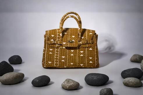 A handcrafted Moroccan fabric tote bag with a geometric pattern in mustard yellow and white, placed on a neutral background surrounded by small stones.