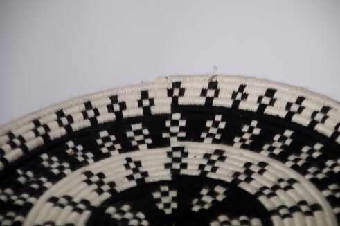 A handcrafted Moroccan coil basket with a geometric black and white design, placed on a neutral background with small stones surrounding it.