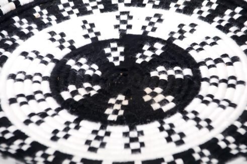 A handcrafted Moroccan coil basket with a geometric black and white design, placed on a neutral background with small stones surrounding it.