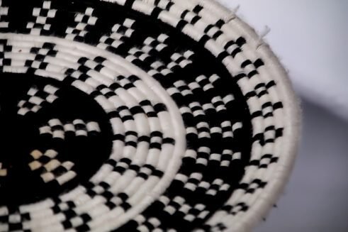 A handcrafted Moroccan coil basket with a geometric black and white design, placed on a neutral background with small stones surrounding it.