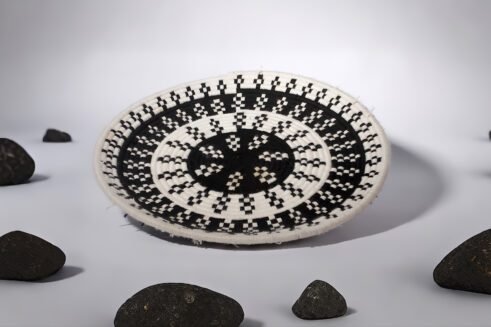 A handcrafted Moroccan coil basket with a geometric black and white design, placed on a neutral background with small stones surrounding it.