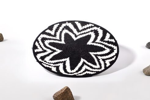 A handcrafted Moroccan coil basket featuring a bold black and white star pattern, placed on a neutral background with small stones surrounding it.