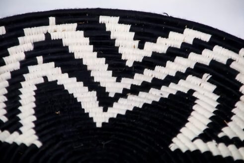 A handcrafted Moroccan coil basket featuring a bold black and white star pattern, placed on a neutral background with small stones surrounding it.