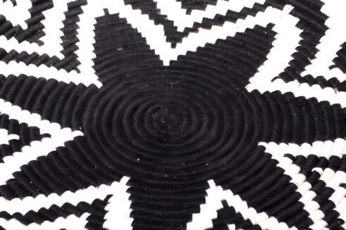A handcrafted Moroccan coil basket featuring a bold black and white star pattern, placed on a neutral background with small stones surrounding it.