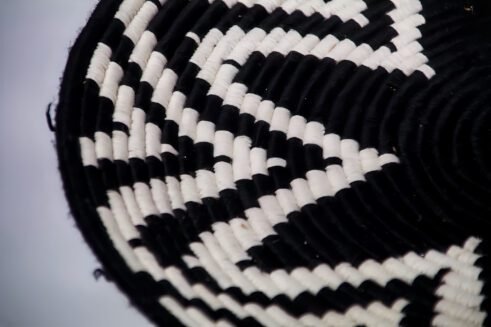 A handcrafted Moroccan coil basket featuring a bold black and white star pattern, placed on a neutral background with small stones surrounding it.